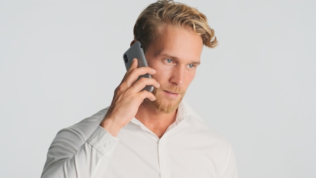 Bel homme barbu en chemise à parler avec son partenaire commercial sur smartphone sur blanc