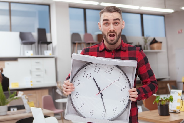 Bel homme barbu à débordé, tenant une grande horloge murale au magasin de meubles