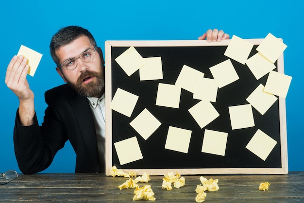 Un bel homme barbu à lunettes tient un tableau de rappel homme triste en vêtements décontractés prenant des notes sur