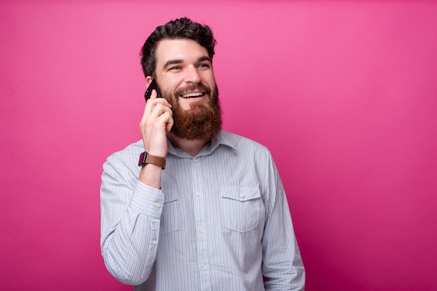 Bel homme barbu parlant au téléphone sur fond rose avec espace de copie.