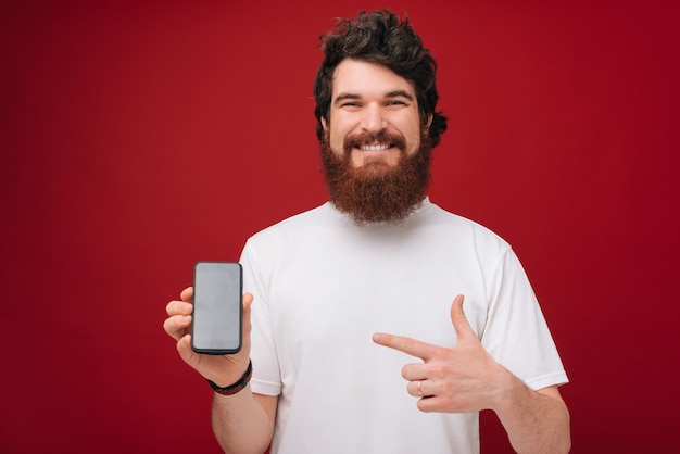 Un bel homme barbu pointant sur mobile tout en souriant à pleines dents