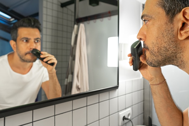 Bel homme barbu se rase le visage avec une tondeuse