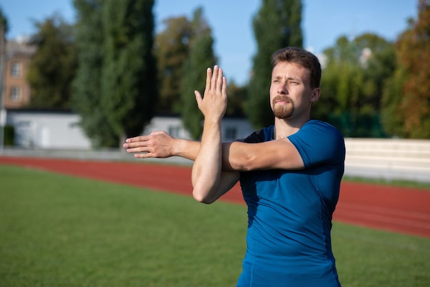 Un bel homme barbu se réchauffe avant l'entraînement au stade. Espace pour le texte