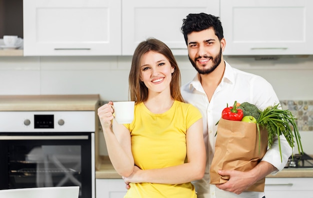 Bel homme barbu tenant un sac à provisions avec des aliments nutritifs sains en chemise blanche immaculée et une femme mince en t-shirt jaune