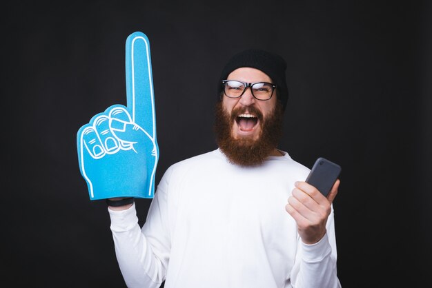 Bel homme barbu tient excité un gant de fan et un smartphone.