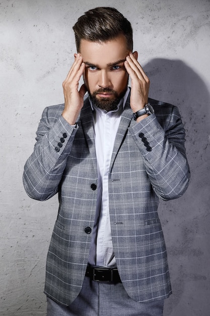 Bel homme barbu vêtu d'un costume à carreaux gris pose contre le mur de béton