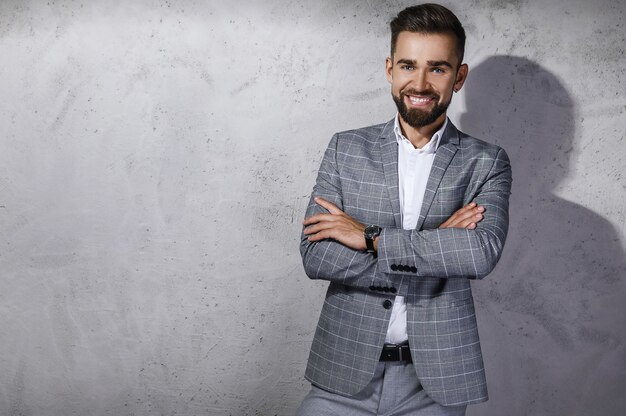 Bel homme barbu vêtu d'un costume à carreaux gris pose contre le mur de béton