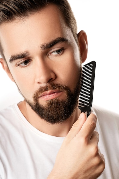 Bel homme bien soigné peignant sa barbe sur fond blanc