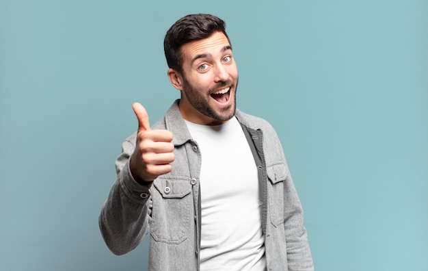 Bel homme blond adulte se sentant fier, insouciant, confiant et heureux, souriant positivement avec le pouce levé