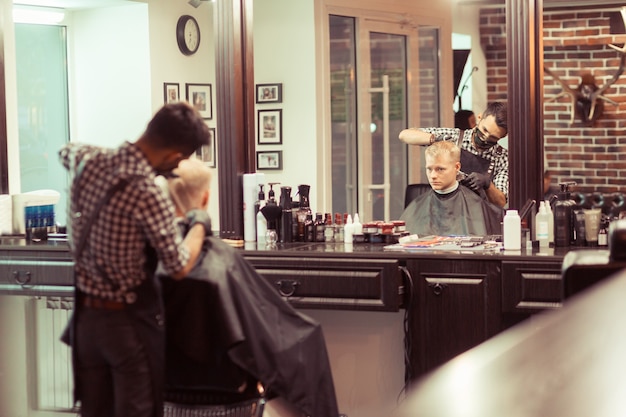 Bel homme blond ayant ses cheveux coupés par le coiffeur au salon de coiffure rétro