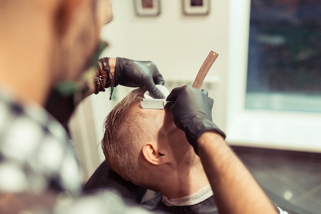 Bel homme blond ayant ses cheveux coupés par le coiffeur au salon de coiffure rétro