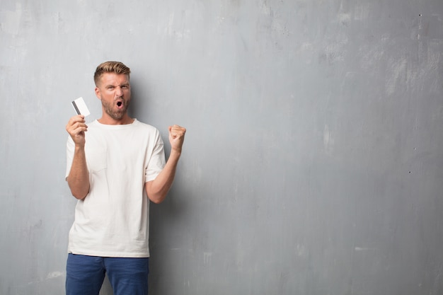 Bel homme blond avec une carte de crédit sur un mur de grunge textur