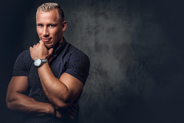 Photo bel homme blond dans une chemise bleu foncé posant sur fond gris dans un studio.