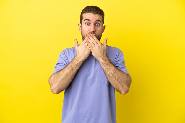 Bel homme blond sur fond jaune isolé couvrant la bouche avec les mains