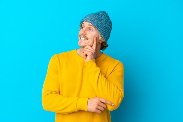 Bel homme blond isolé sur un mur bleu en pensant à une idée tout en levant les yeux