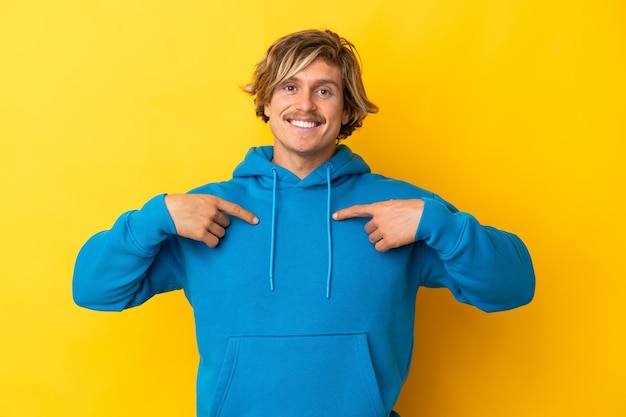 Bel homme blond isolé sur un mur jaune avec une expression faciale surprise