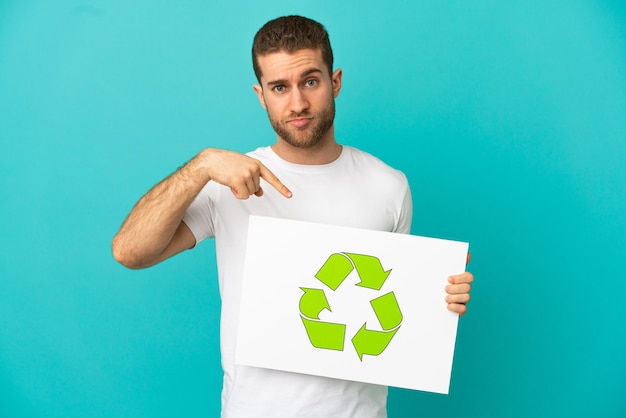 Photo bel homme blond isolé tenant une pancarte avec l'icône de recyclage et la pointant