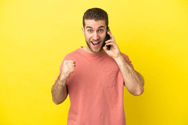 Bel homme blond utilisant un téléphone portable sur fond isolé célébrant une victoire en position de vainqueur