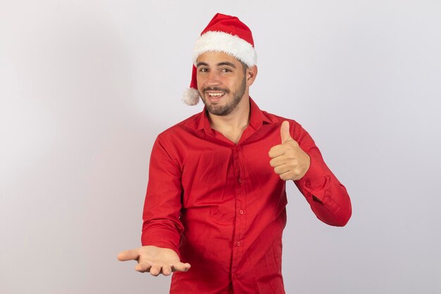 Bel homme en bonnet de noel tendre la main avec quelque chose avec le pouce vers le haut signe ok