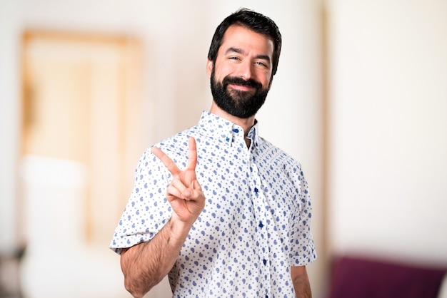 Bel homme brune avec une barbe faisant le geste de la victoire