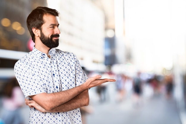 Bel homme brune avec une barbe présentant quelque chose