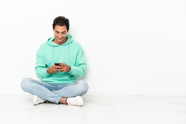 Bel homme caucasien assis sur le sol envoyant un message avec le mobile