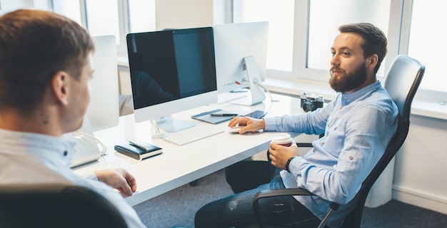 Bel homme caucasien, boire un café a un dialogue avec son collègue au bureau.