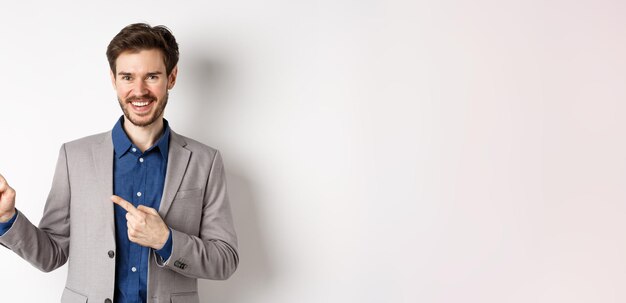 Bel homme caucasien en costume d'affaires pointant du doigt la bannière et souriant montrant des publicités
