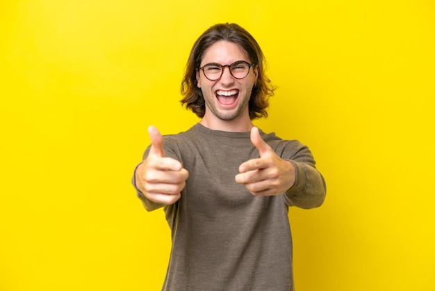 Bel homme caucasien isolé sur fond jaune pointant vers l'avant et souriant