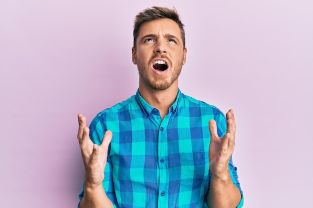 Bel homme caucasien portant des vêtements décontractés fous et fous criant et hurlant avec une expression agressive et les bras levés concept de frustration