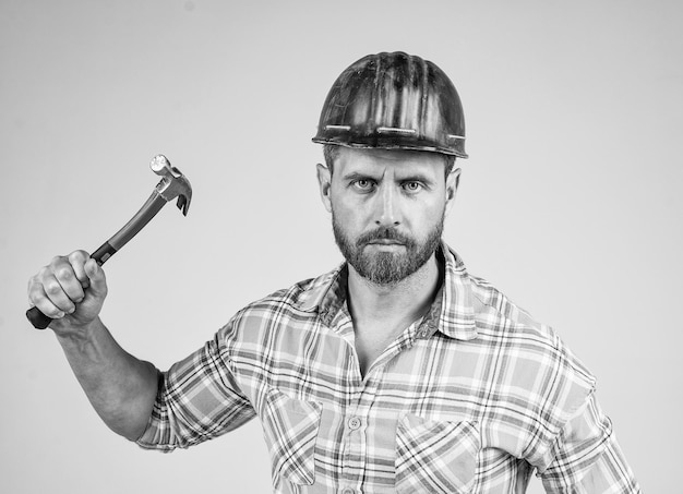 Bel homme charpentier en casque de sécurité de construction et chemise à carreaux sur chantier avec entretien de marteau