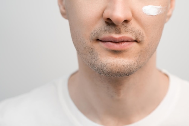 Un bel homme avec un chaume dans un t-shirt blanc un échantillon d'une crème pour le visage sur sa joue