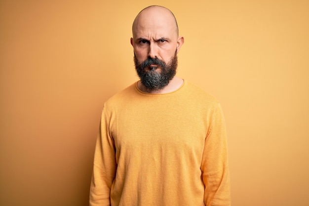 Bel homme chauve avec barbe portant un pull décontracté debout sur fond jaune sceptique et nerveux fronçant les sourcils contrarié à cause du problème Personne négative