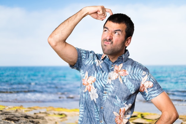 Bel homme avec une chemise à fleurs ayant des doutes à la plage