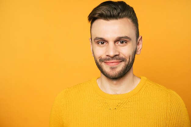 Un bel homme confiant en jaune pose sur fond orange et regarde la caméra