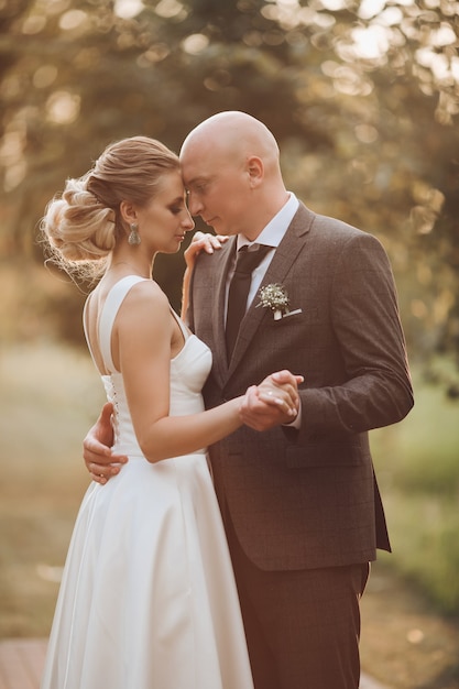 Bel homme en costume noir et chemise blanche se détend dans le jardin avec sa jolie femme aux cheveux blonds en robe blanche