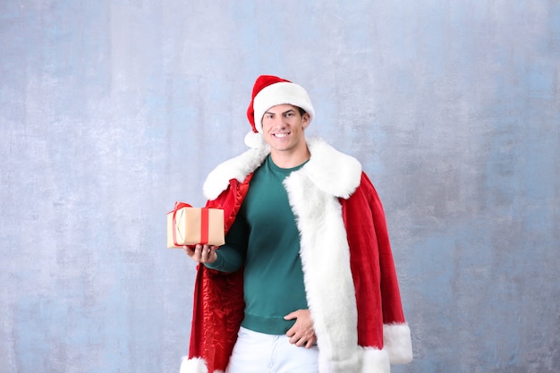 Bel homme en costume de père Noël tenant une boîte-cadeau sur fond de couleur