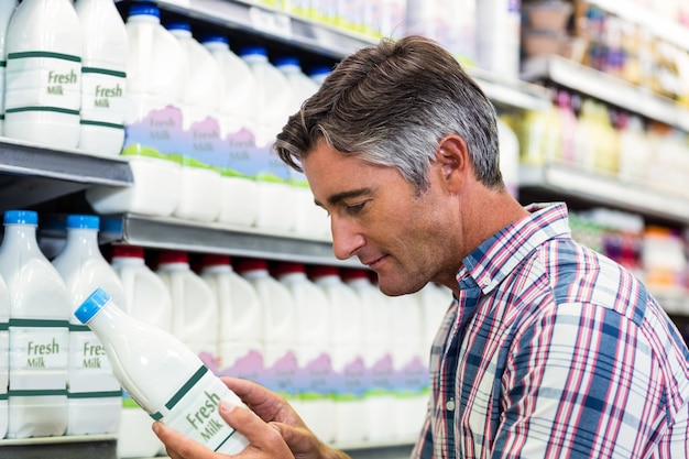 Bel homme dans le supermarché en regardant la bouteille de lait