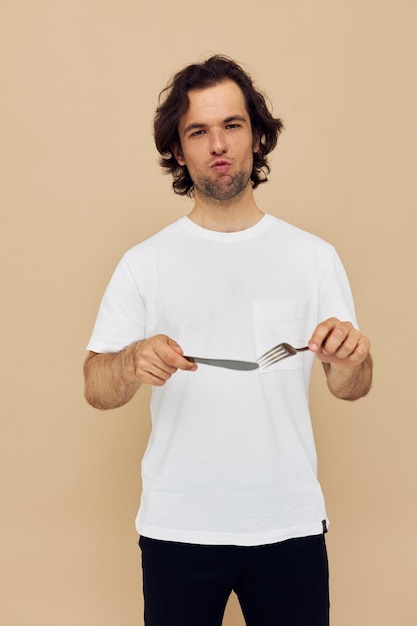 Bel homme dans un T-shirt blanc avec un couteau avec une fourchette fond beige