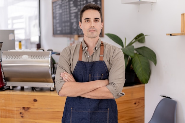 Un bel homme debout dans un café, c'est un employé de café, il se prépare à ouvrir un magasin pour servir les clients, un employé ouvre un magasin pour servir de la nourriture et des boissons. Concept de service de restauration.