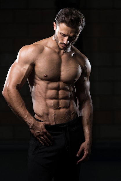 Bel homme debout fort dans la salle de gym et flexion des muscles musclé athlétique bodybuilder modèle de remise en forme posant après les exercices