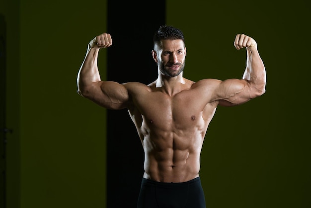 Bel homme debout fort dans la salle de gym et flexion des muscles musclé athlétique bodybuilder modèle de remise en forme posant après les exercices