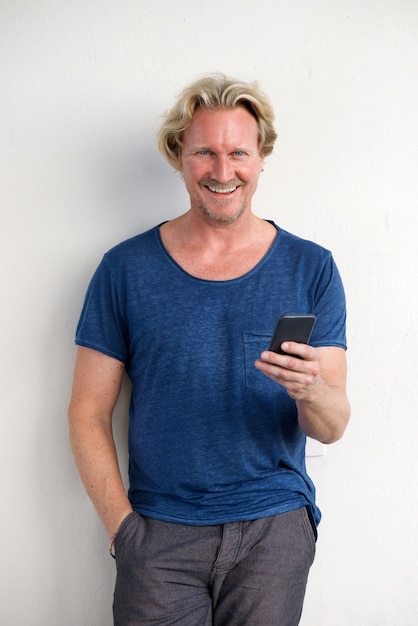 Bel homme debout par un mur blanc avec un téléphone portable