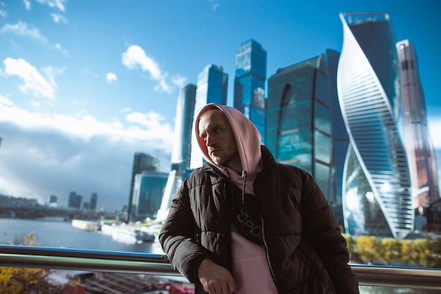 Bel homme décontracté en veste noire et sweat à capuche rose debout sur une vue de gratte-ciel. Ville de Moscou.