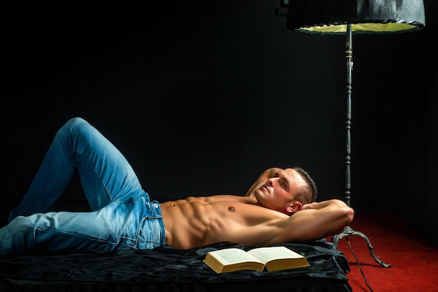 Bel homme en denim bleu avec livre et torse nu Allongé sur le lit et se détendre Mode de vie de luxe