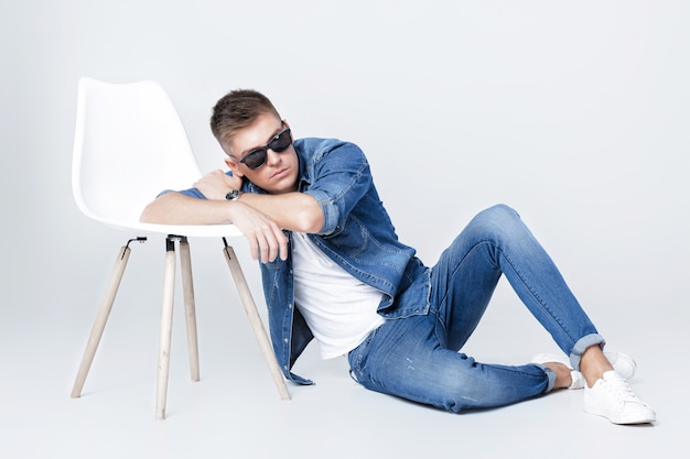 Bel homme en denim pose près de chaise blanche