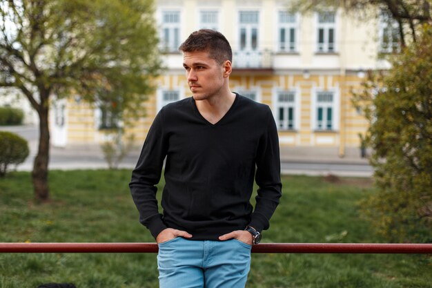 Bel homme élégant dans un T-shirt noir et un pantalon bleu, à l'extérieur