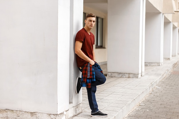 Bel homme élégant tenant une chemise et pose près du mur blanc.