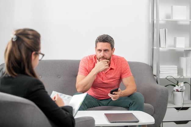 Bel homme est assis sur un canapé et parle au psychologue. Une patiente en psychologie parle de sa santé mentale lors d'une consultation psychologique. Crise de l'homme d'âge moyen.