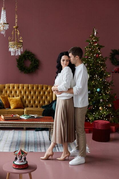 Bel homme étreignant une belle femme aux cheveux longs tout en posant à l'intérieur décoré pour Noël